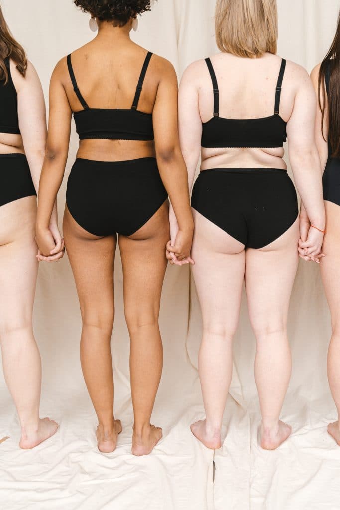 A back view of women with various body types in underwear holding hands A view behind several women of various body types in comfortable black underwear, holding hands.
